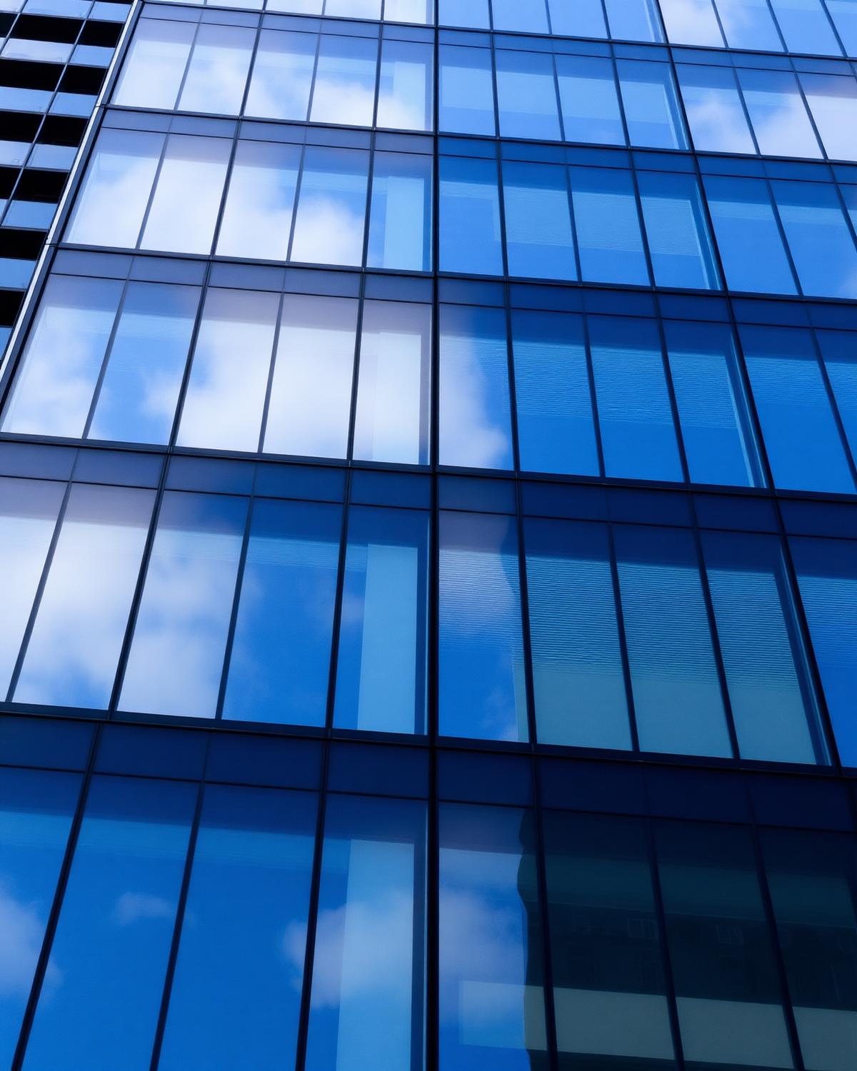 Modern glass office building facade reflecting the sky